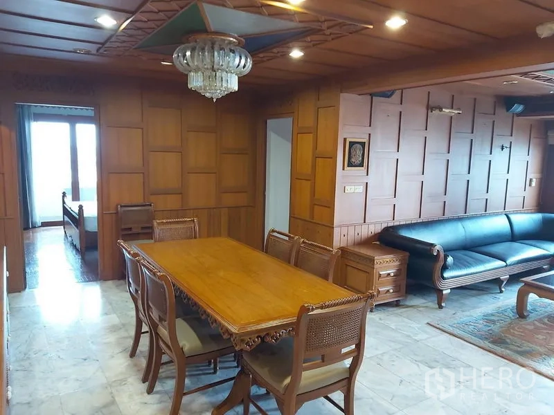 Condominium for rent in Samphanthawong, Bangkok - Wood‑paneled dining room with chandelier, carved table set, and adjacent living area with sofa.