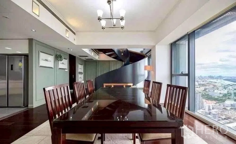 Condominium for rent in Sathon, Bangkok - Formal dining area beside floor-to-ceiling windows and a sculptural spiral staircase with sweeping city skyline views.