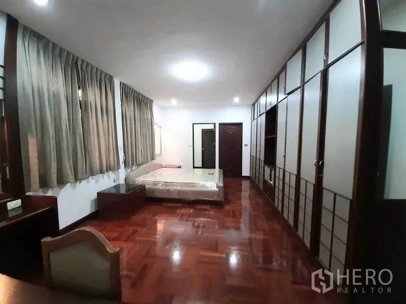 独立式住宅 出租在Watthana, Bangkok - 宽阔卧室，成排衣柜、床与木地板。