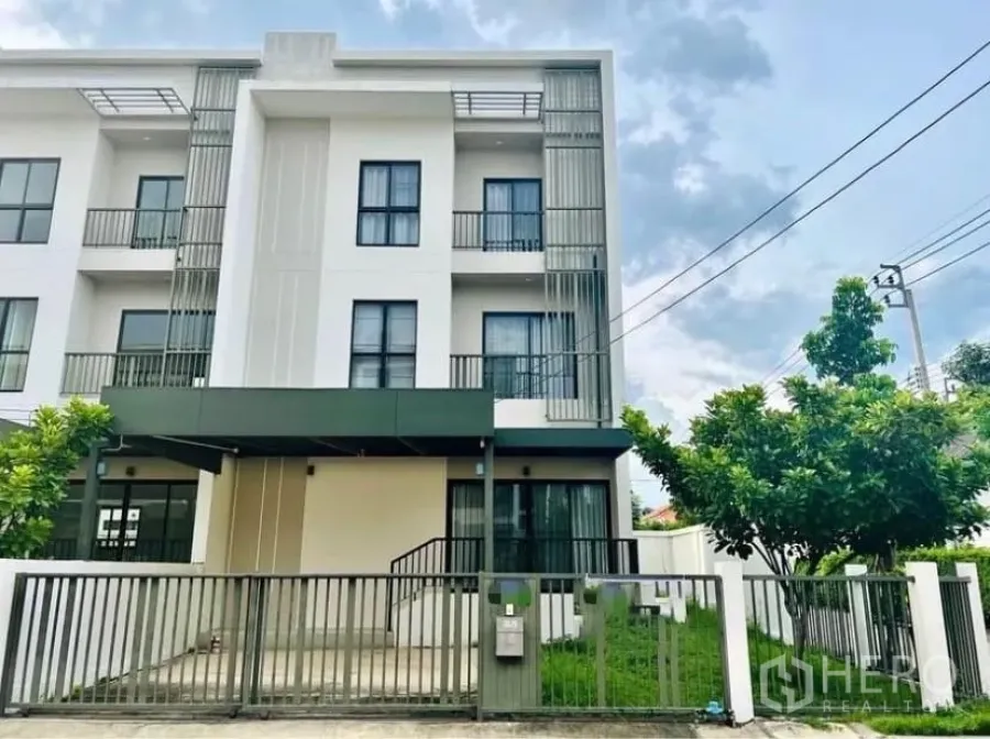 Townhouse for rent in Saphan Sung, Bangkok - Modern three-storey end-unit townhouse with balconies, gated carport and small front lawn.