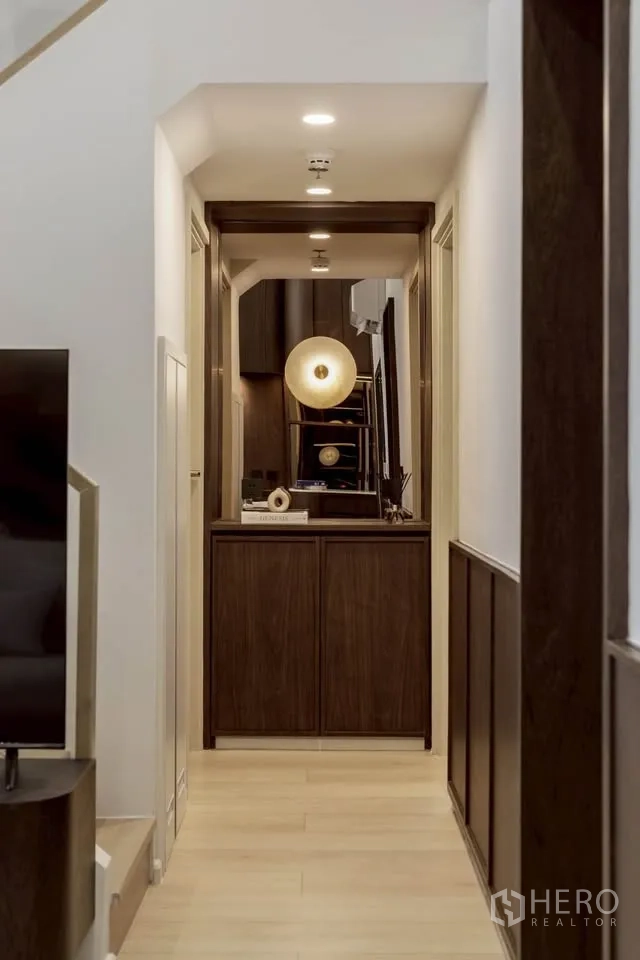 Condominium for rent in Khlong Toei, Bangkok - Corridor with wooden cabinet and ambient lighting leading to living space.