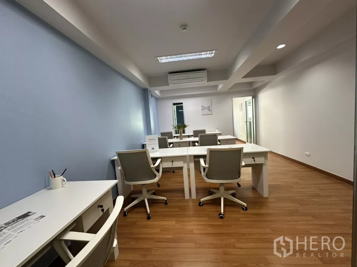 Office Space for rent in Watthana, Bangkok - Open-plan Thonglor office with white desks and grey chairs on wood flooring, blue accent wall and ceiling lights.