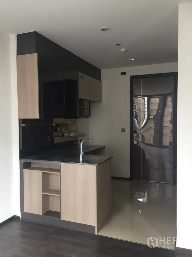 คอนโด ขายในDin Daeng, Bangkok - ครัวคอนโดกะทัดรัด ท็อปหินสีดำ ตู้ลายไม้ และประตูทางเข้าในยูนิตสมัยใหม่ย่านดินแดง
