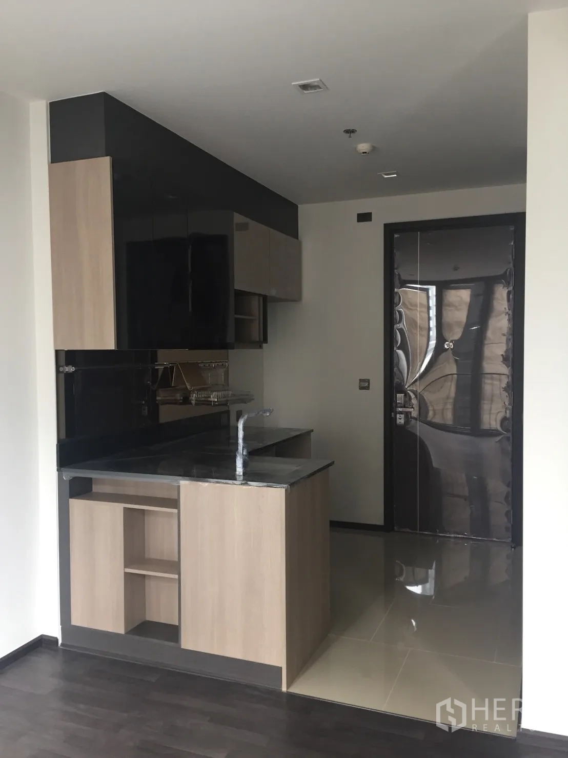 คอนโด ขายในDin Daeng, Bangkok - ครัวคอนโดกะทัดรัด ท็อปหินสีดำ ตู้ลายไม้ และประตูทางเข้าในยูนิตสมัยใหม่ย่านดินแดง