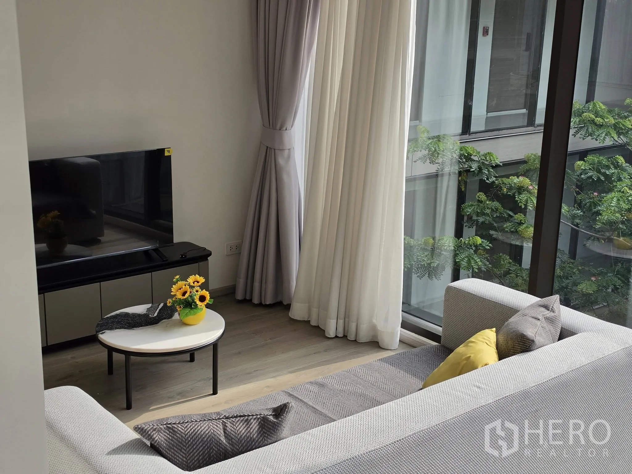 Condominium for rent in Khlong Toei, Bangkok - Bright living room with sofa, TV console, coffee table and floor-to-ceiling window facing greenery.