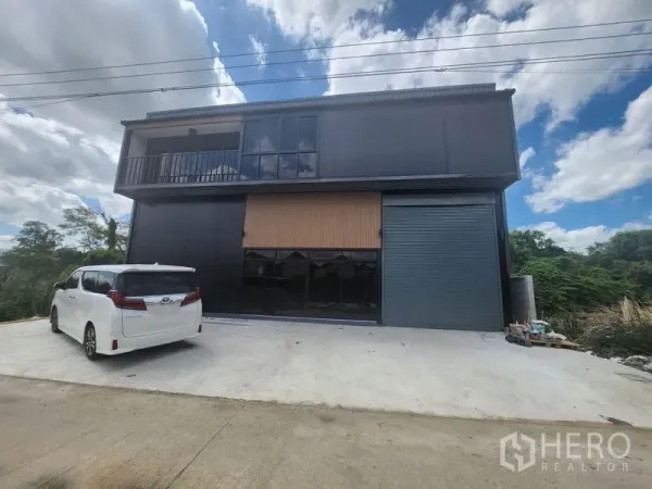 คลังสินค้า ให้เช่าหรือขายในLam Luk Ka, Pathum Thani - ด้านหน้าโกดังสองชั้นโทนสีดำสมัยใหม่ มีระเบียง กระจกบานใหญ่ และประตูม้วน พร้อมลานคอนกรีตจอดรถ