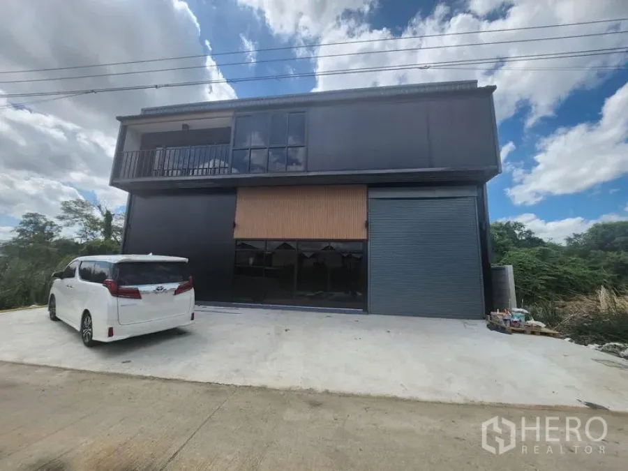 คลังสินค้า ให้เช่าหรือขายในLam Luk Ka, Pathum Thani - ด้านหน้าโกดังสองชั้นโทนสีดำสมัยใหม่ มีระเบียง กระจกบานใหญ่ และประตูม้วน พร้อมลานคอนกรีตจอดรถ