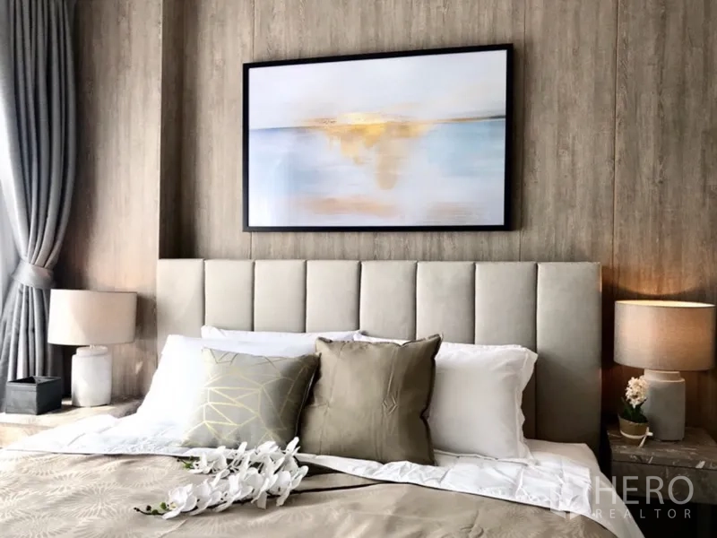 Condominium for rent or sale in Pathum Wan, Bangkok - Close-up of a stylish bed with tufted headboard, bedside lamps, grey curtains and abstract artwork.