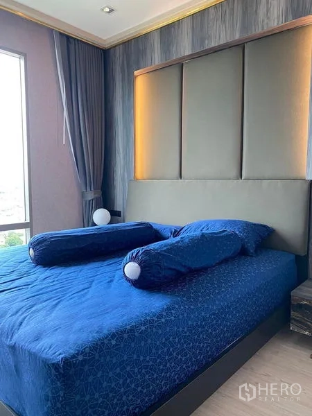 Condominium for sale in Bang Kho Laem, Bangkok - Master bedroom with upholstered headboard, blue bedding and corner window.