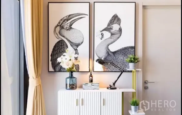 公寓 出租在Phra Khanong, Bangkok - 装饰矮柜与黑白装饰画，旁有落地窗帘。