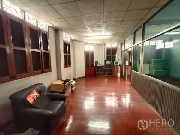 Shophouse for rent in Sathon, Bangkok - Open office or living area with timber floor, sofa and cabinets beside a glass partition.