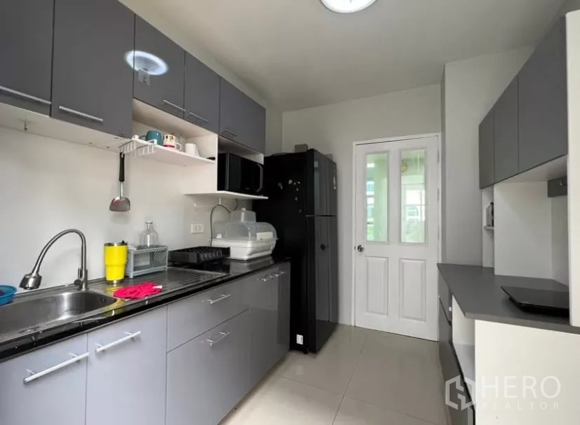 Detached House for rent or sale in Prawet, Bangkok - Enclosed kitchen with grey cabinetry, black countertop and appliances.