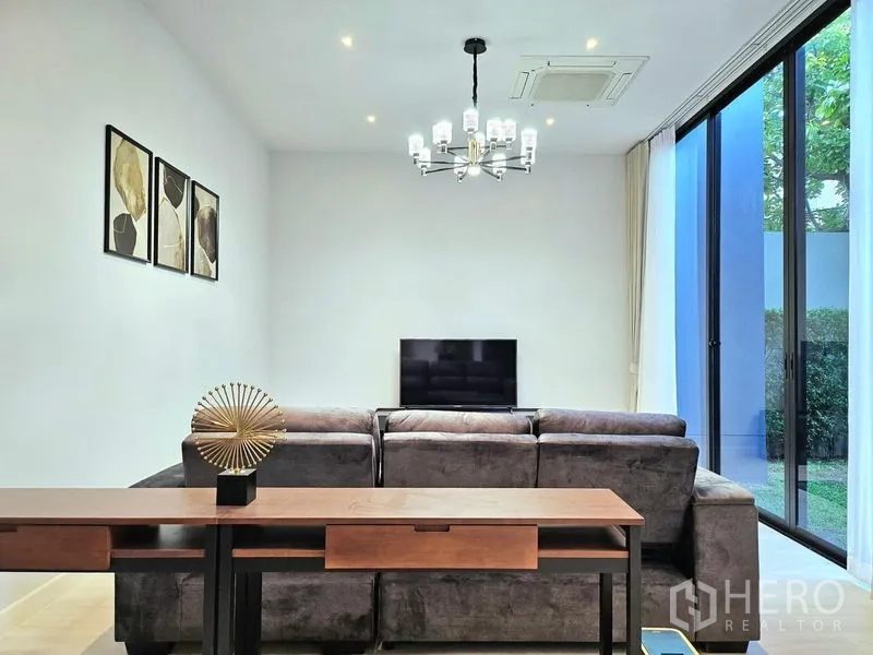 Detached House for rent in Bang Kapi, Bangkok - Living room with gray sectional sofa, TV and sliding glass doors to garden