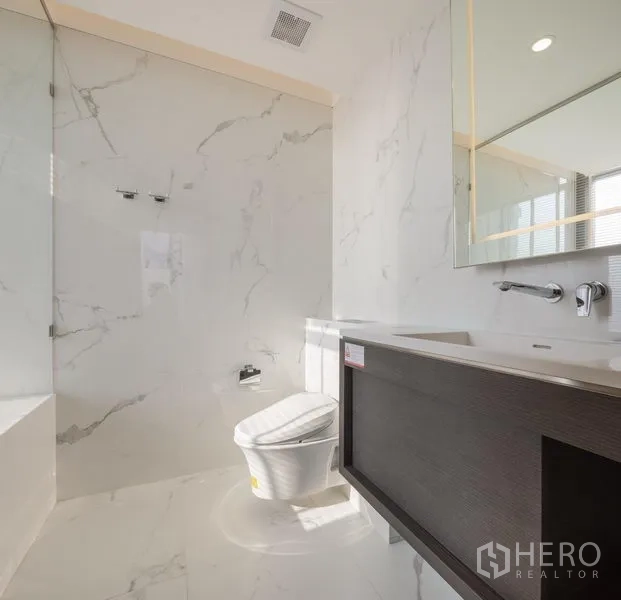 Condominium for rent in Khlong Toei, Bangkok - Bright bathroom with floating vanity, illuminated mirror, and marble walls.
