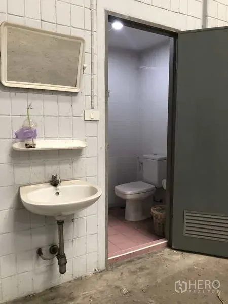Warehouse for rent in Lat Lum Kaeo, Pathum Thani - Restroom close-up with pink floor tiles, sink and toilet inside the warehouse.