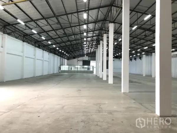 货栈 出租在Nonthaburi - 仓库中央通道视角，整齐立柱、带保温层的屋顶和明亮的白色墙面。