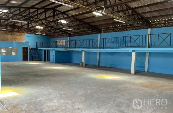 Warehouse for rent in Sai Noi, Nonthaburi - Spacious warehouse interior with steel truss roof, blue walls, and a long mezzanine with railings.
