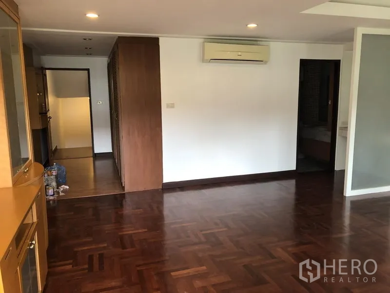 Townhouse for rent or sale in Watthana, Bangkok - Master bedroom with parquet flooring, built-in wardrobes and a wall-mounted air conditioner.