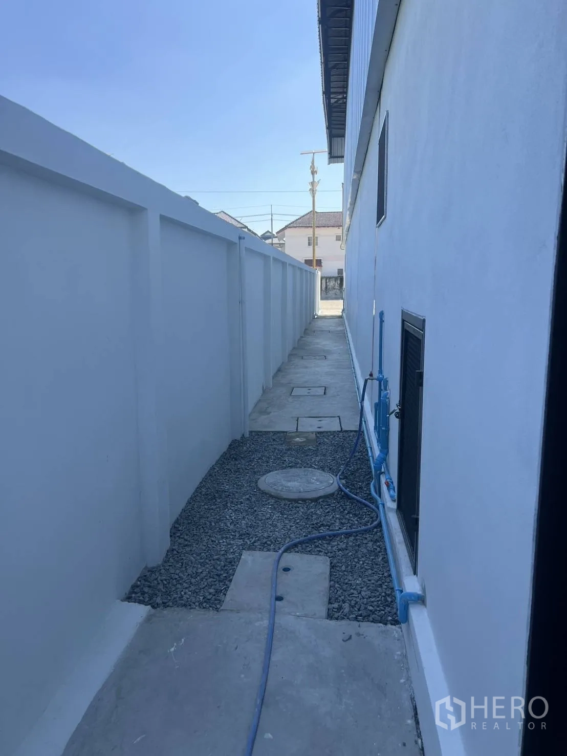 Warehouse for rent in Bang Phli, Samut Prakan - Exterior service walkway along the building with utility piping and a gravel base.