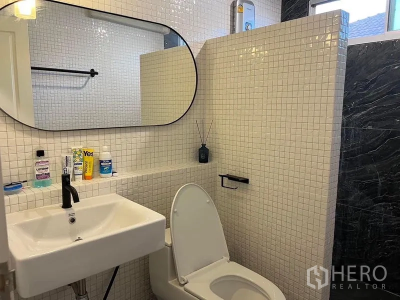 独立式住宅 出售在Bang Kruai, Nonthaburi - 卫生间白色马赛克墙，椭圆镜面，黑色龙头与坐便器。