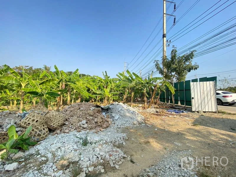 Land for sale in Bang Khae, Bangkok - Gate area beside the main road with banana trees and construction rubble at the corner of the plot.