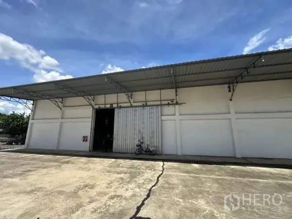 货栈 出租在Mueang Pathum Thani, Pathum Thani - 巴吞他尼仓库外观，超大混凝土装卸场、金属滑门与遮雨棚屋顶，蓝天下清晰可见。