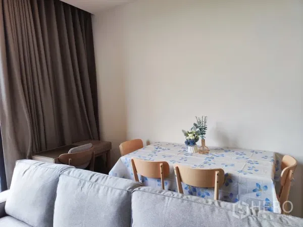 Condominium for rent in Watthana, Bangkok - Four-seat dining table with floral cover and a small work desk near tall curtains.