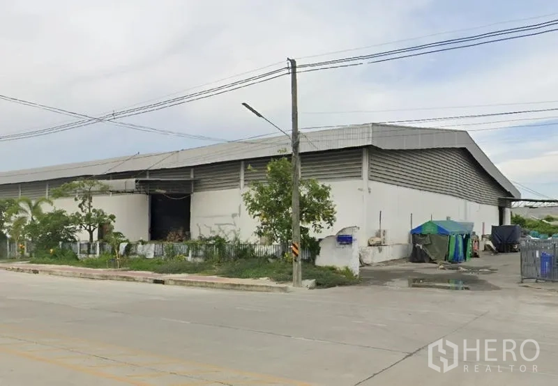 Warehouse for rent in Bang Pakong, Chachoengsao - Corner exterior of the warehouse with fenced greenery, service yard and roadside frontage.
