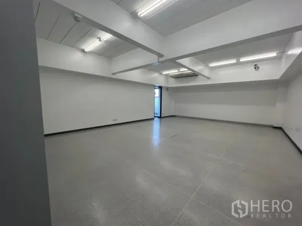 Office Space for rent in Mueang Samut Prakan, Samut Prakan - Spacious workspace with exposed ceiling beams, fluorescent lights, and a side exit door.