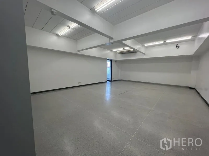 Office Space for rent in Mueang Samut Prakan, Samut Prakan - Spacious workspace with exposed ceiling beams, fluorescent lights, and a side exit door.