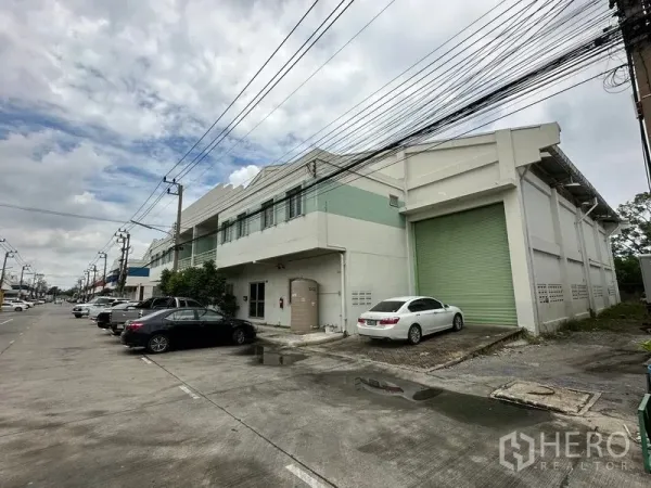 工厂 出租在Khlong Luang, Pathum Thani - 工业区内两层工厂外观，配大型绿色卷帘装卸门与前方停车位。