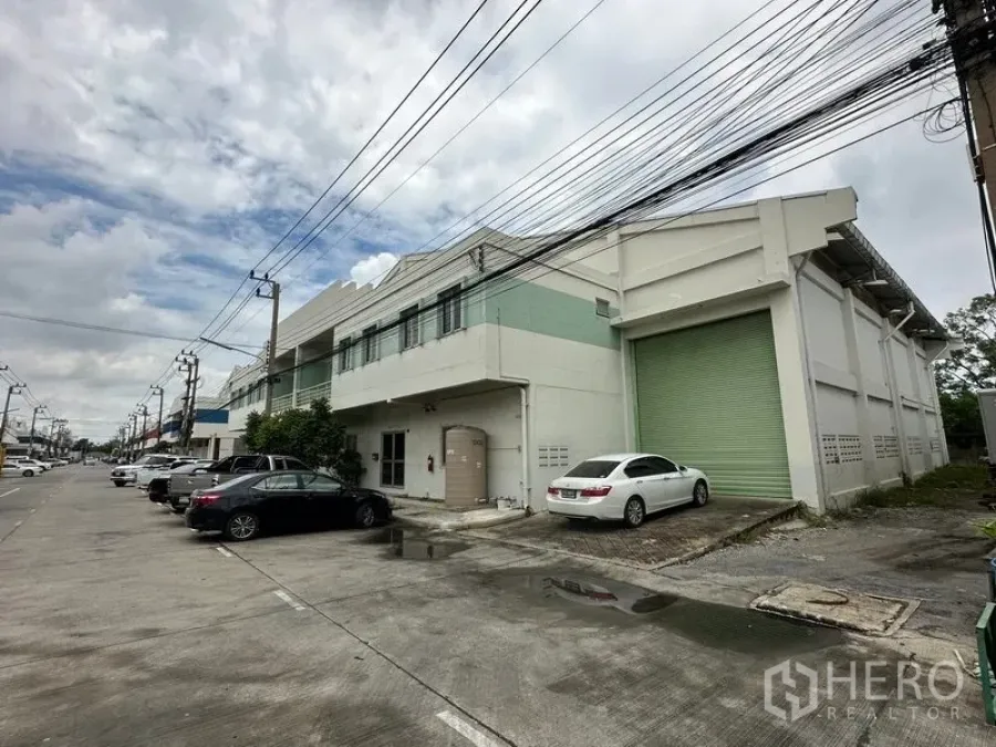 โรงงาน ให้เช่าในKhlong Luang, Pathum Thani - มุมมองริมถนนของโรงงานสูงสองชั้น พร้อมประตูม้วนสีเขียวขนาดใหญ่และที่จอดรถในแถบอุตสาหกรรม