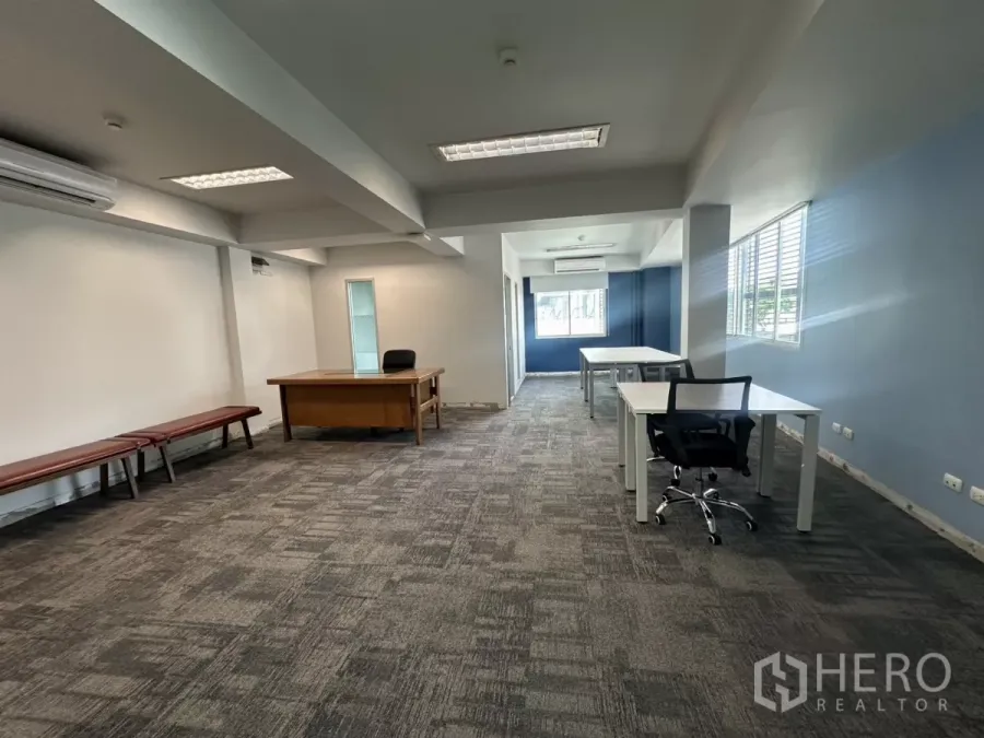 Office Space for rent in Watthana, Bangkok - Open-plan Thonglor office interior with gray carpet, blue accent wall, desks and large windows.