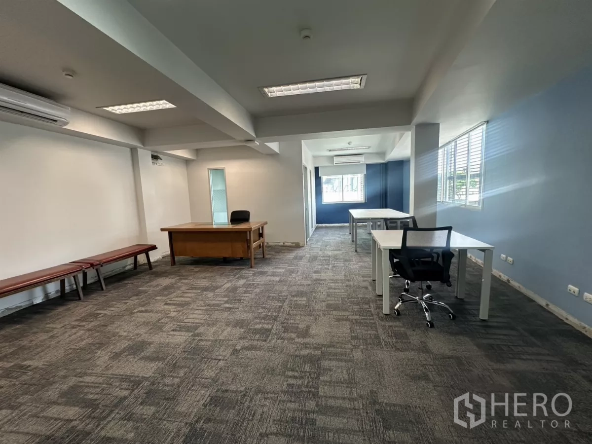 Office Space for rent in Watthana, Bangkok - Open-plan Thonglor office interior with gray carpet, blue accent wall, desks and large windows.