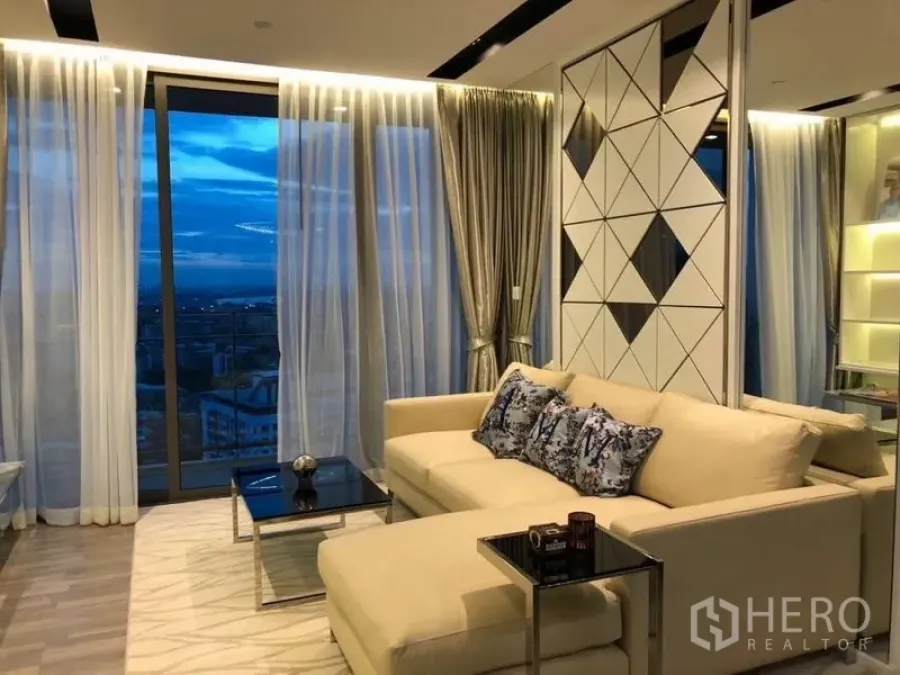 Condominium for rent or sale in Watthana, Bangkok - Elegant living room with sheer curtains, sectional sofa and blue hour city view.