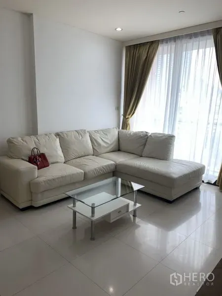 Condominium for rent or sale in Khlong Toei, Bangkok - Corner with white sectional sofa by floor-to-ceiling windows and sheer curtains, plus a glass coffee table.