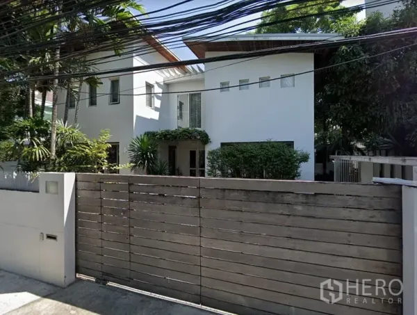 Detached House for rent in Chatuchak, Bangkok - Modern two-storey white detached house behind a wooden gate with mature greenery.