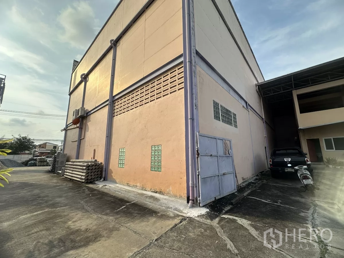 Warehouse for rent in Mueang Nonthaburi, Nonthaburi - Side elevation of the warehouse with service gate, ventilation glass blocks and concrete yard.