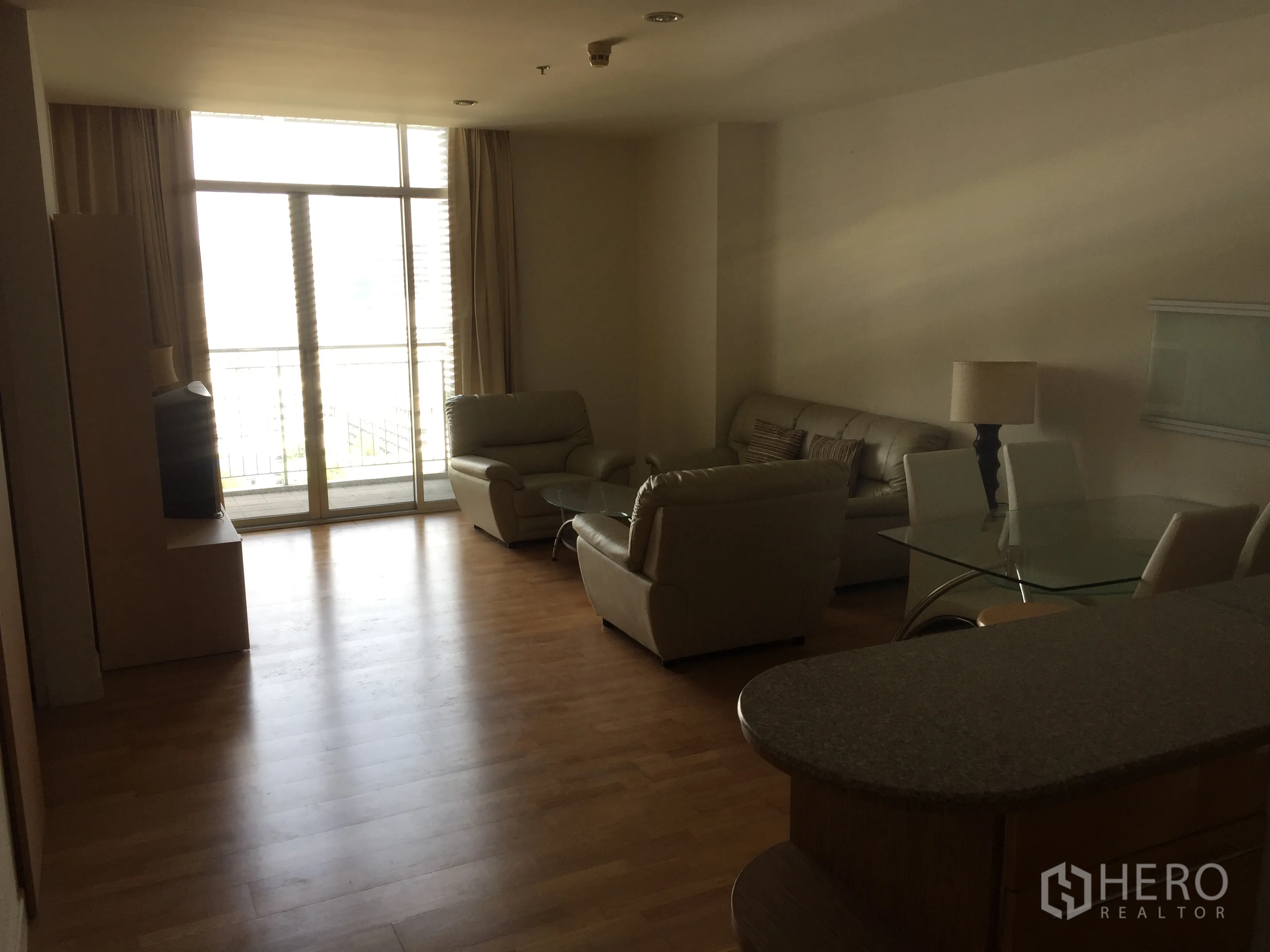 Condominium for rent in Sathon, Bangkok - Bright living room with floor-to-ceiling sliding doors to a balcony, leather sofas, glass dining table, and an open kitchen counter on wood flooring.