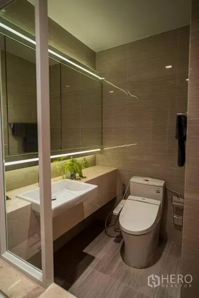 คอนโด ให้เช่าในWatthana, Bangkok - ห้องน้ำร่วมสมัยพร้อมกระจกไฟซ่อน อ่างล้างหน้าติดผนัง และโถสุขภัณฑ์บนพื้นกระเบื้อง