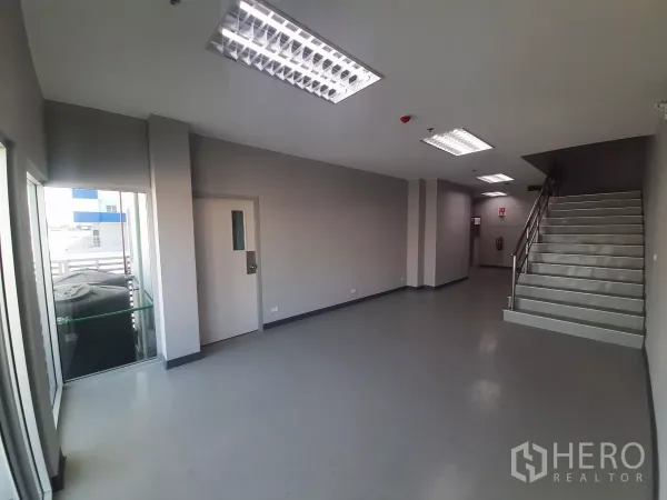 Factory for rent in Bang Lamung, Chon Buri - Ground-floor office lobby with staircase, glass door to a balcony and grey flooring.