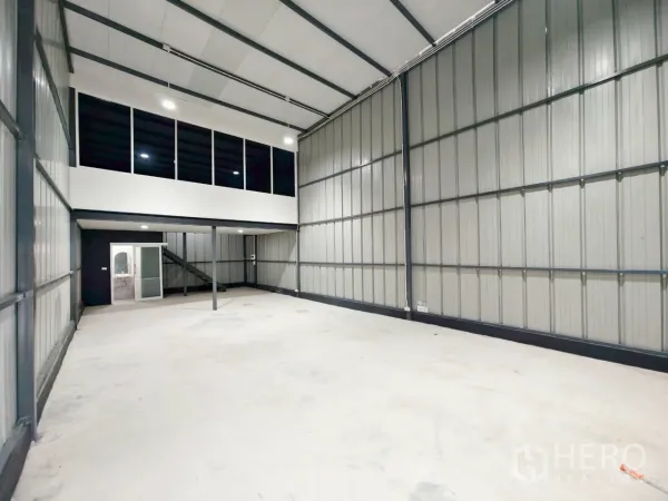 Warehouse for rent in Phra Khanong, Bangkok - Spacious storage bay showing steel wall panels and a mezzanine office above.