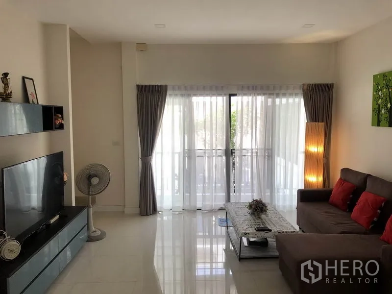 Townhouse for rent in Saphan Sung, Bangkok - Bright living room with sofa, TV console and full-height sliding glass doors with sheer curtains
