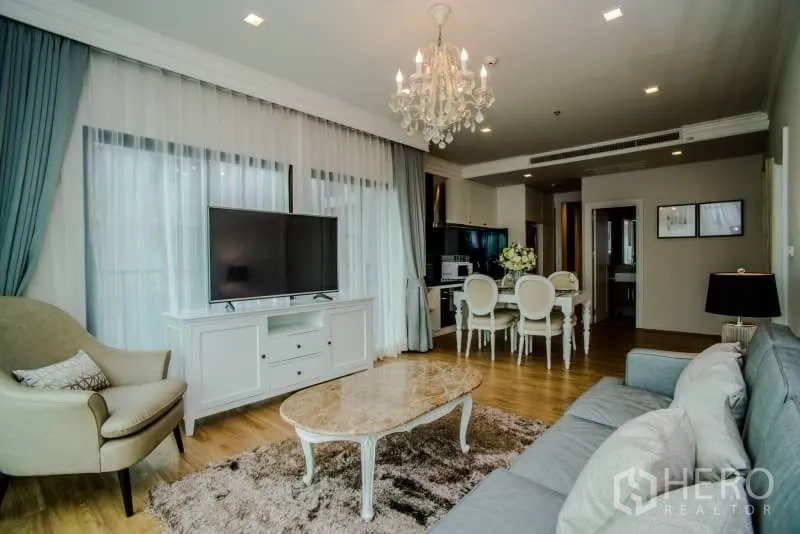 Condominium for rent or sale in Watthana, Bangkok - Elegant living room with sofa, TV console, marble coffee table, and sheer curtains.