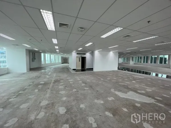 Office Space for rent - Wide office area with columns, bright fluorescent lighting and continuous windows along the facade.
