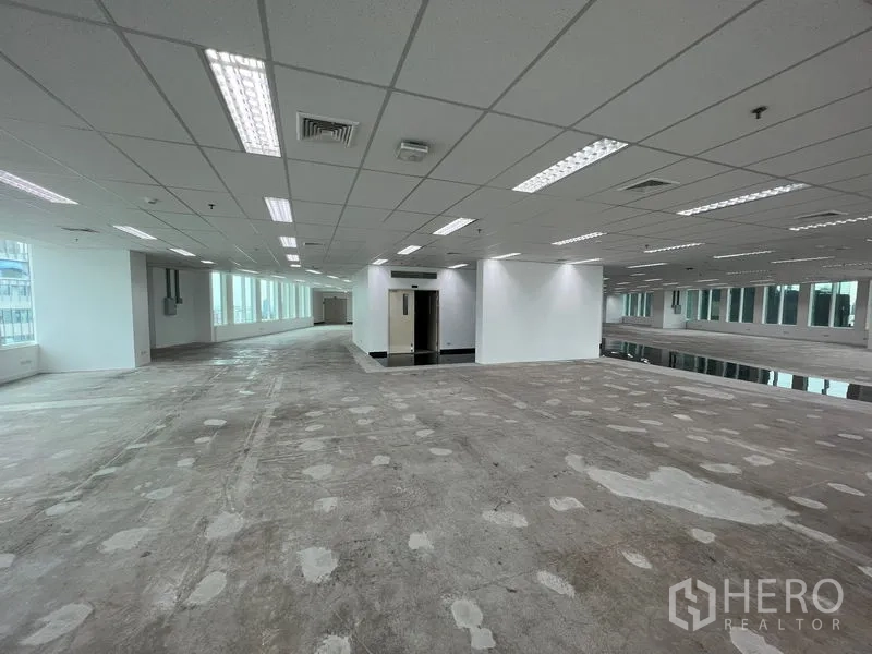 Office Space for rent - Wide office area with columns, bright fluorescent lighting and continuous windows along the facade.