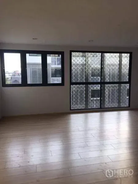 Townhouse for sale in Yan Nawa, Bangkok - Sunlit living area with light wood floors and large windows with security screens in a Bangkok townhouse.