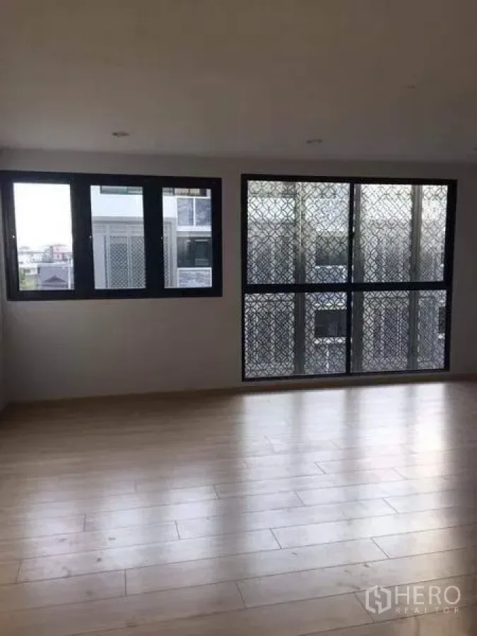 Townhouse for sale in Yan Nawa, Bangkok - Sunlit living area with light wood floors and large windows with security screens in a Bangkok townhouse.