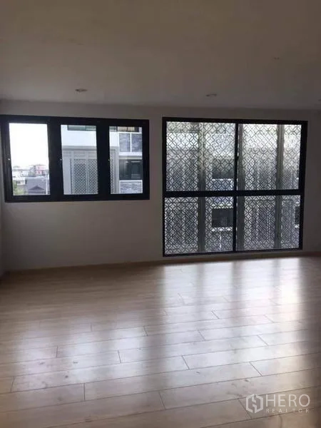 Townhouse for sale in Yan Nawa, Bangkok - Sunlit living area with light wood floors and large windows with security screens in a Bangkok townhouse.