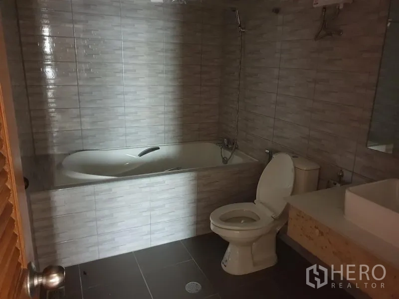 Condominium for rent in Watthana, Bangkok - Bathroom with bathtub, toilet and vanity finished with gray wall tiles.
